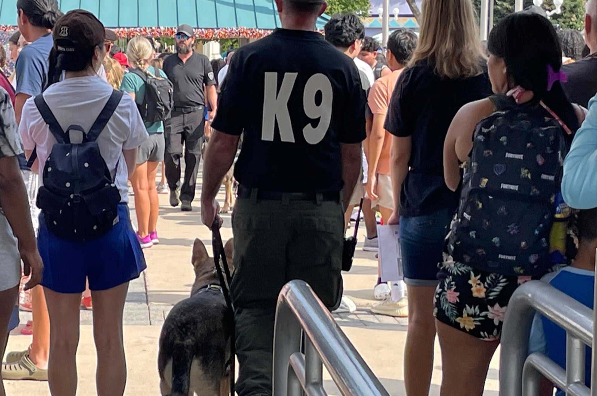 a man wearing a k9 shirt walking a dog in a crowd
