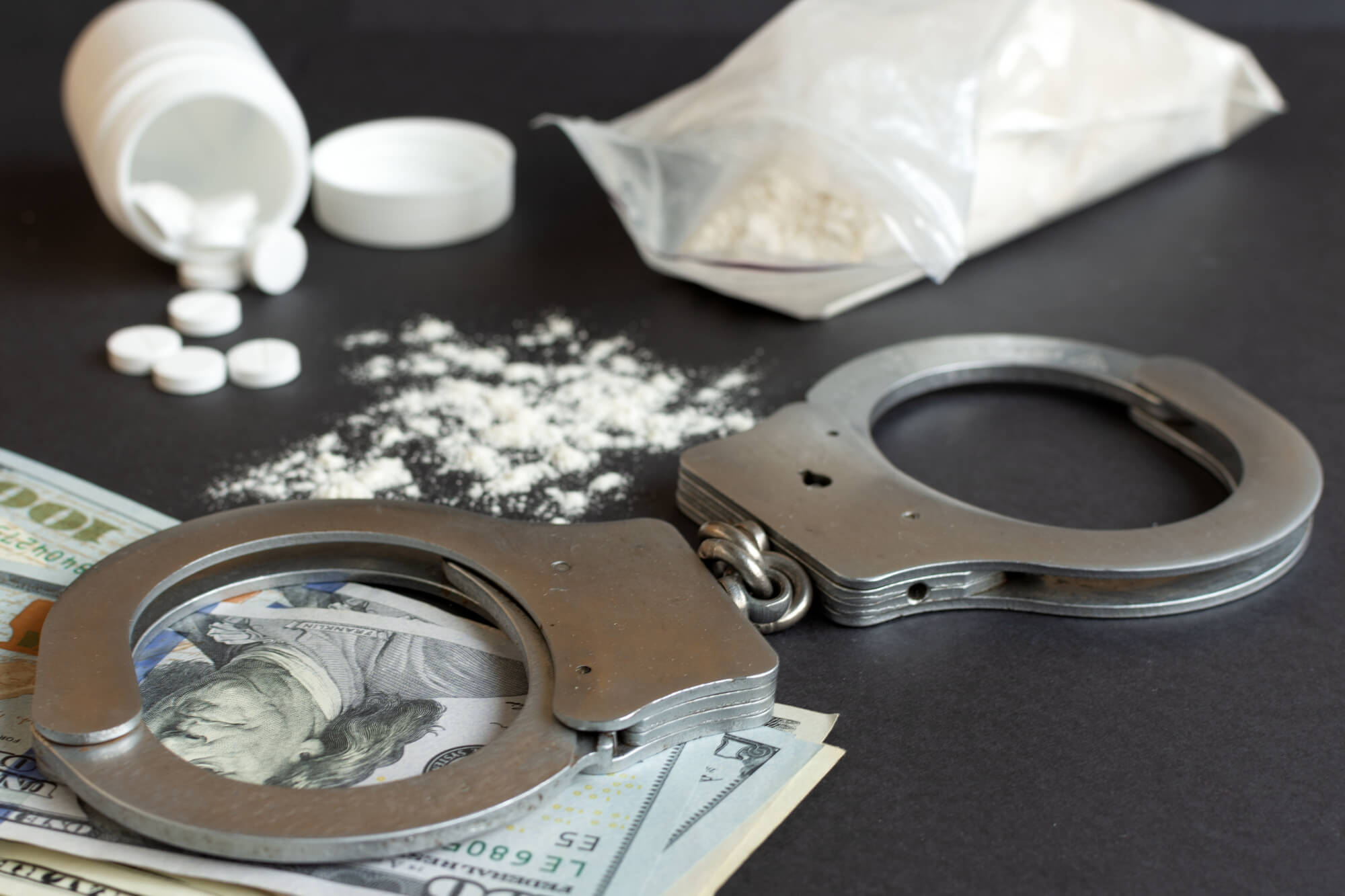 a pair of handcuffs sitting on top of a pile of money next to white powder and white pills
